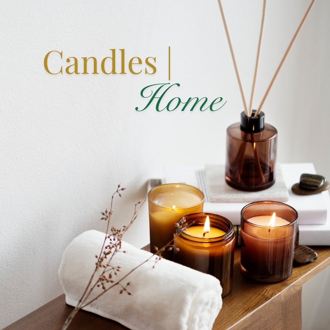 Candles and home gift collection with burning soy candles, reed diffuser, rolled towel, and decorative accents on a wooden table.