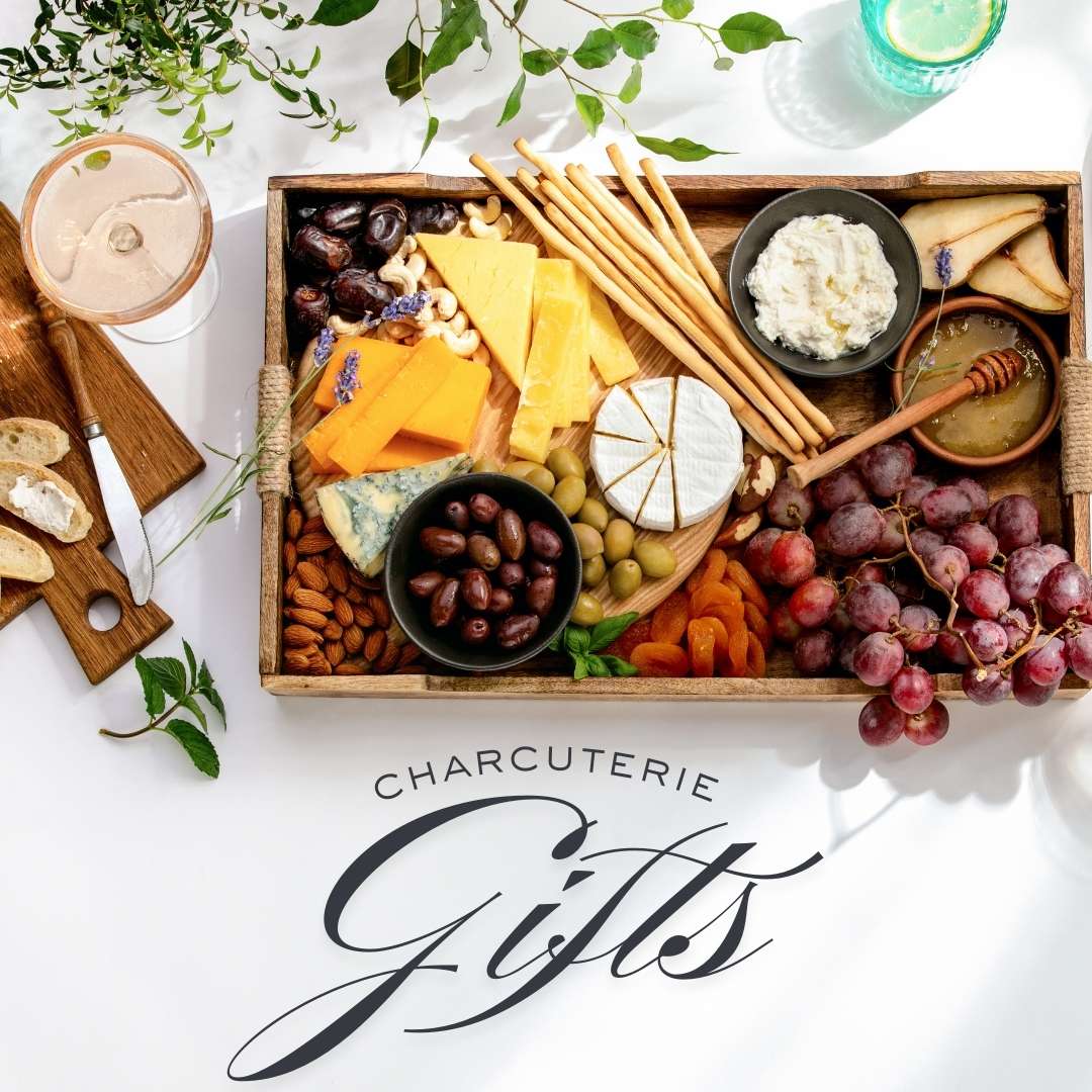 Charcuterie gift set with assorted cheeses, olives, nuts, grapes, breadsticks, dried fruit, and honey arranged in a wooden tray.
