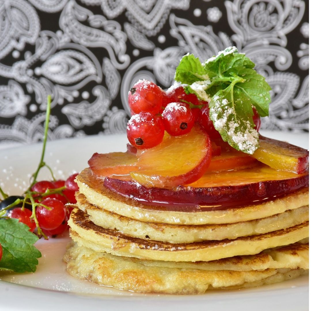 pancakes with syrup and grapes and sliced apples on top on a plate