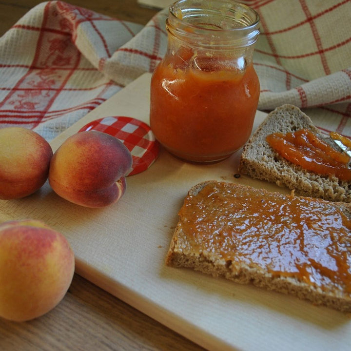 preach preserves on toast settin on a board plank with peaches and a jar of peach preserves