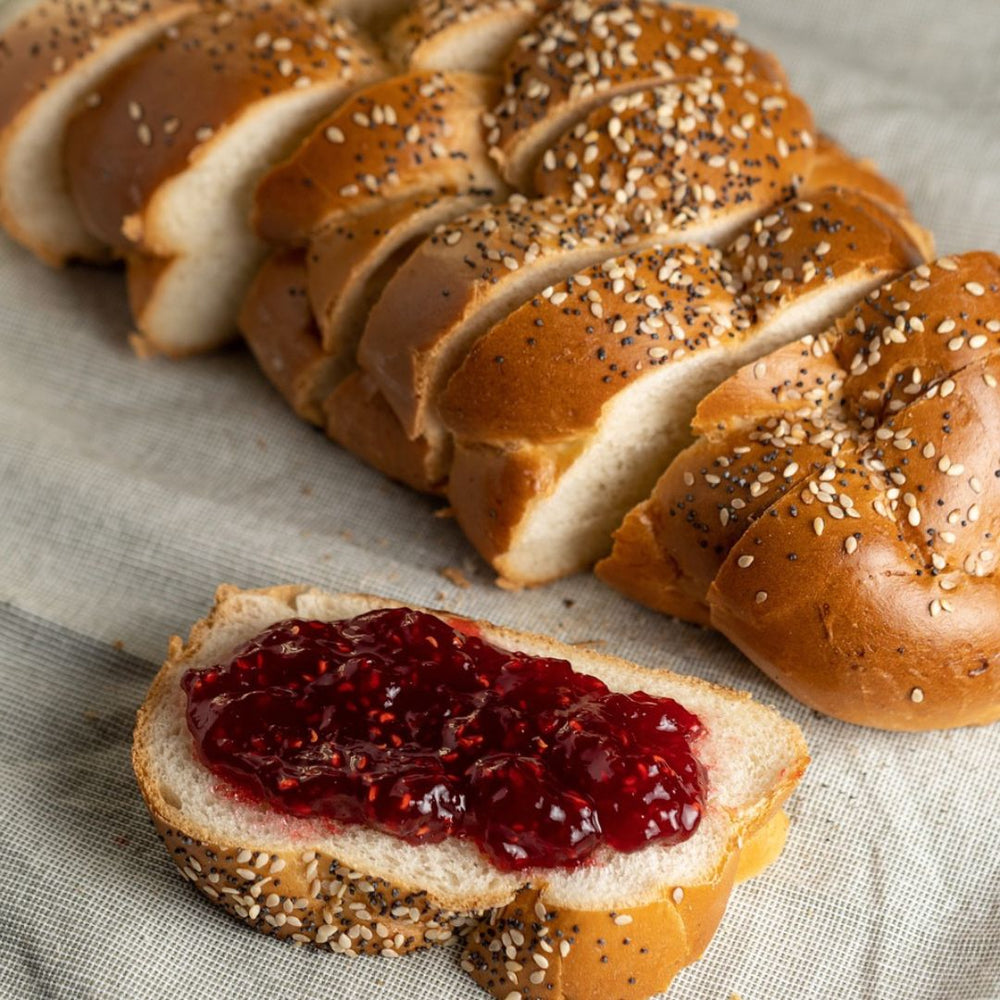 Strawberry Preserves on a slice of bread with a loaf of bread next to it setting on a table cloth