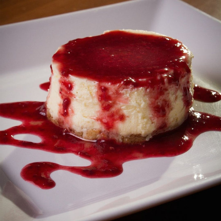 strawberry preserves on a round cheesecake on a white plate.